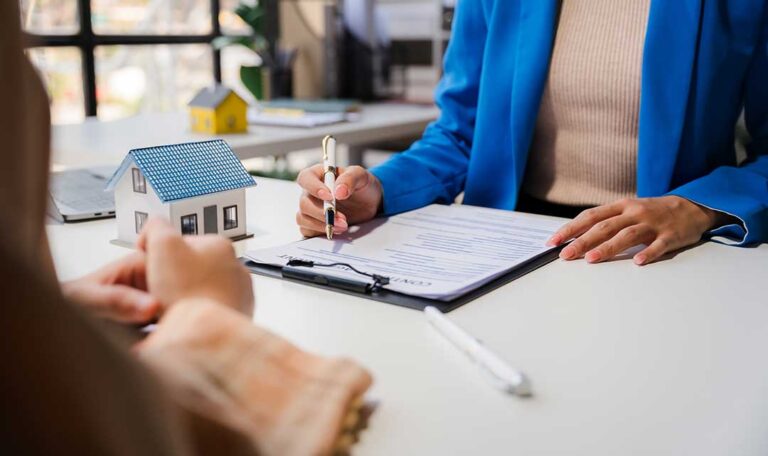 A person reviews a health insurance policy booklet while sitting at a kitchen table with a cup of tea.
