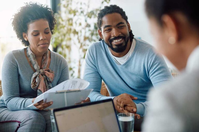 Adults review a life insurance denial letter and medical documents at a kitchen table.